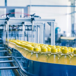 Photo of yellow plastic soda bottles filling the conveyor belt of a plastic bottle filling machine